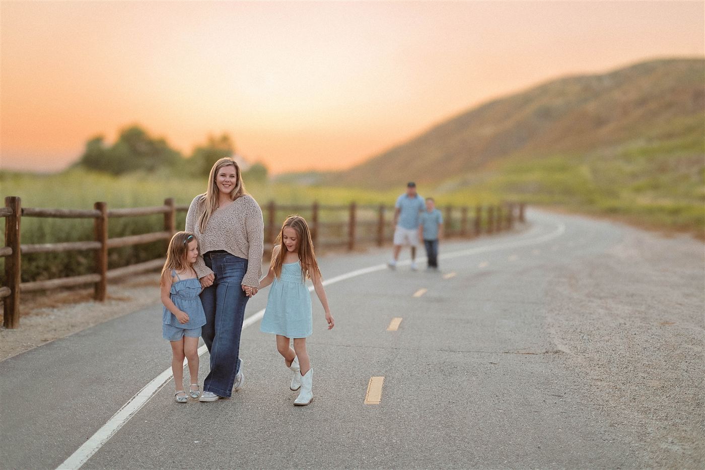 Mother walking hand in hand with her two daughters on a trail at sunset, with dad and son following behind