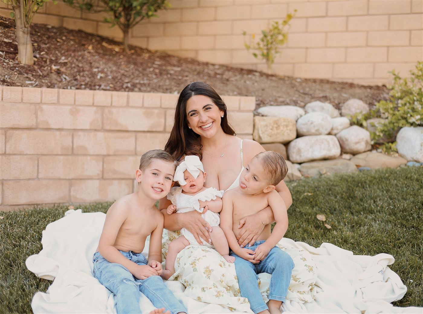 The Berner family, a smiling mother on a blanket in the backyard with her two young sons and baby daughter